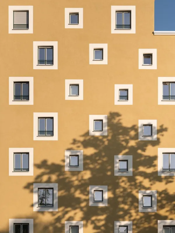 Großer Ausschnitt eines gelben Wohngebäudes mit Schatten eines Baumes.