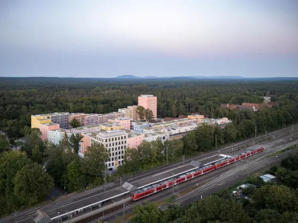 Blick von oben auf das Regensburger Viertel mit den Gleisen und dem S-Bahnhof im Vordergrund. Man sieht eine durchfahrende S-Bahn.