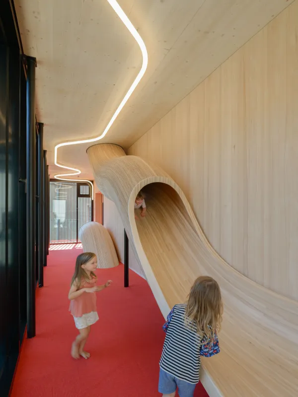 Rutsche aus Holz mit rotem Teppich und Beleuchtung mit spielenden Kindern.
